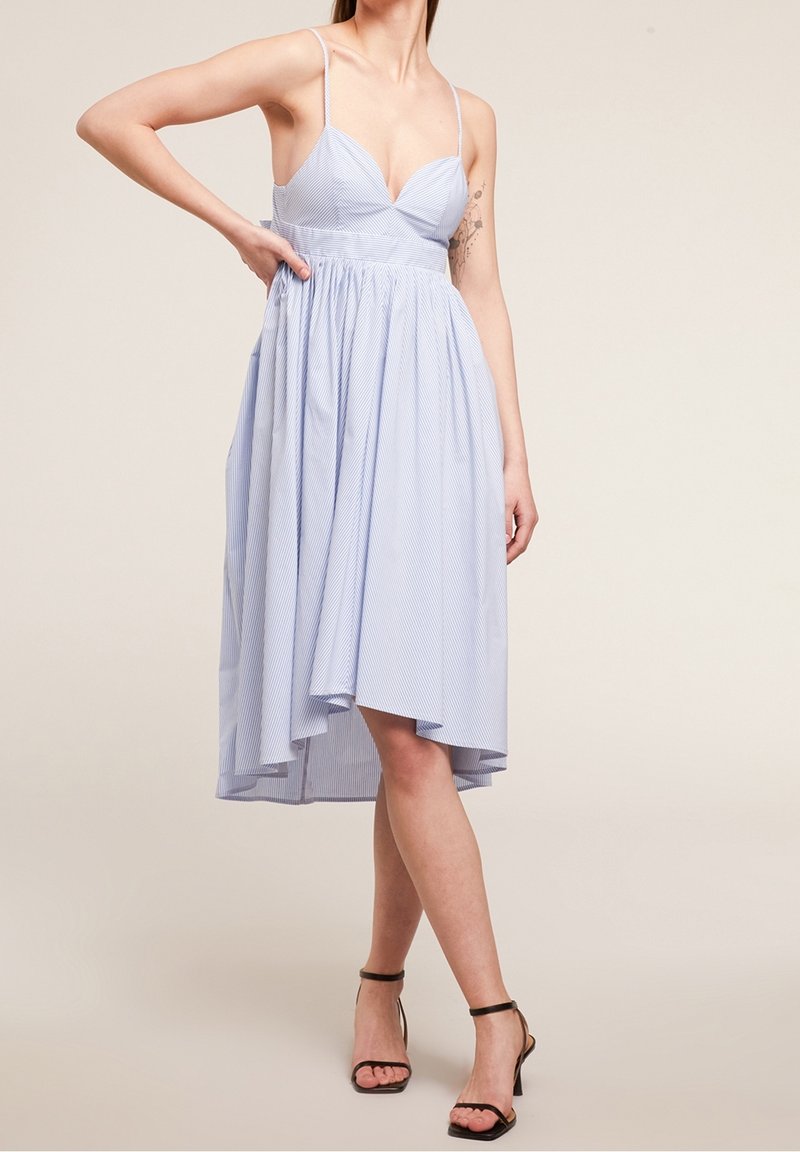 Robe rayée bleu clair avec un corsage ajusté, des bretelles spaghetti et une jupe évasée, présentant un ourlet asymétrique et une texture de tissu douce.