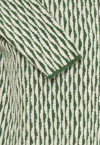 Gros plan sur un tissu en laine texturé avec des rayures verticales irrégulières vertes et blanches alternées et une section de manche repliée.