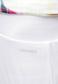 Pantalones cortos de tela blanca con una textura suave, con la marca "climalite" sutilmente impresa cerca de la cintura. Tejido colorido y con estampados parcialmente visible.
