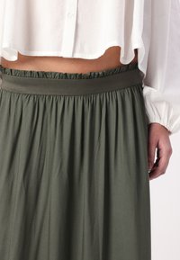 Jupe verte olive en tissu froncé avec une taille élastique. Un design fluide met en valeur la douceur du tissu et le mouvement.