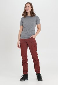 Grå kortärmad skjorta kombinerad med röda cargobyxor med flera fickor. Modellen bär svarta utomhusskor med gummisula.