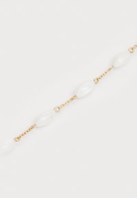 Zlatý reťazec náramku s predĺženými bielymi korálkami prerušovanými článkami. Hladký, lesklý povrch, neutrálna farebná schéma.