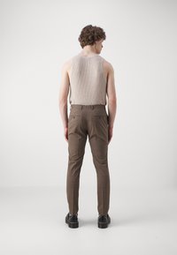 Top de bază bej cu dungi și pantaloni în carouri maro. Pantalonii au buzunare la spate; modelul poartă pantofi negri. Fundal neutru.