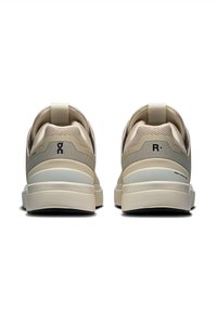 Beige sportskor med ovandel i mesh, vadderad sula och strukturerad bakdetalj. Innehåller dragflikar och logotyp på hälarna.