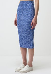 Jupe midi à motifs bleus avec une silhouette ajustée, ceinture élastique et texture côtelée, associée à des baskets blanches.