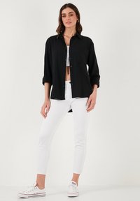 Black button-up shirt with a ribbed texture, single chest pocket, and rolled sleeves, paired with white skinny jeans and white sneakers.