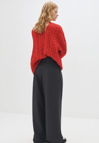Punainen, cable-knit-neule, jossa on ylisuuria siluetteja, yhdistettynä korkeavyötäröisiin harmaisiin suuressa lahkeissa housuihin. Minimalistinen tyyli ja tekstuuriset kuviot.