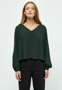 Blusa verde scuro a V con maniche lunghe e chiusura con bottoni. Realizzata in tessuto liscio, presenta un design corto e una caduta morbida.