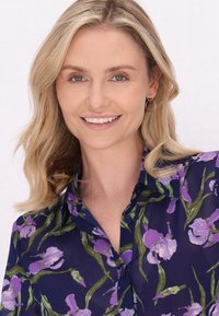 Blusa trasparente navy con stampa floreale viola. Presenta un collo a camicia, maniche corte e chiusura frontale con bottoni, arricchita da dettagli verdi.