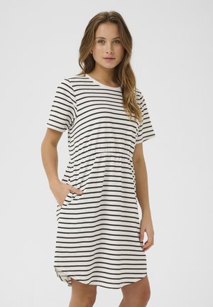 Vestido de manga corta a rayas en algodón blanco y negro. Presenta una cintura fruncida, bolsillos laterales y un dobladillo redondeado con aberturas laterales.