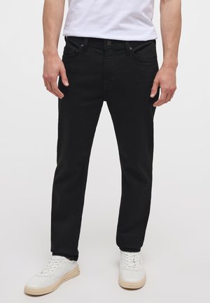 Jeans de mezclilla negra con corte recto, que cuentan con cinco bolsillos, cremallera en la bragueta y una textura sutil. Llevados con zapatillas blancas.