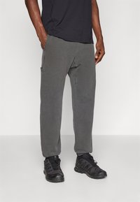 Gray cotton sweatpants with a relaxed fit, side pockets, and subtle stitching details, paired with black athletic shoes.