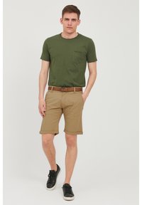 Zielona bawełniana koszulka z kieszonką, zestawiona z beżowymi szortami z podwiniętymi nogawkami. Całość uzupełniają czarne trampki. Prosty i casualowy design.