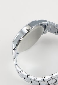 Montre-bracelet en métal argenté avec une finition polie, un boîtier rond et une lunette lisse. Bracelet en maillons métalliques avec des maillons carrés.
