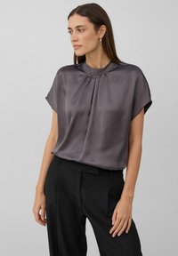 Blouse à manches courtes fluide en satin gris foncé avec un col haut, présentant des plis à l'avant et une texture lisse et douce.