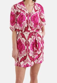Kortärmad klänning i lätt tyg med ett abstrakt mönster i rosa och vitt, med v-ringning, bälte i midjan och sidofickor.