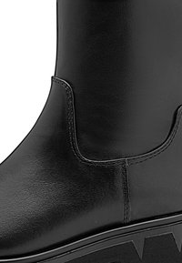 Black leather ankle boot featuring a smooth, glossy finish, subtle stitching, and a textured rubber sole with angular patterns.