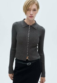 Grå ribbet cardigan med lange ærmer og kravehals, der har en frontlukning med metalliske knapper og en åben bunden. 