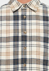 Geruit overhemd met licht IVORY, marineblauwe en oranje patronen. Heeft een button-down kraag, zes knopen, en een borstzak. Van katoen.