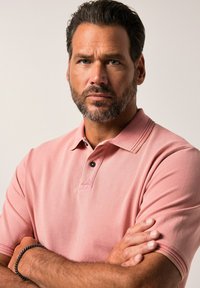 Lichtroze poloshirt met een textuurafwerking, voorzien van een drukknoopsluiting met drie knopen en donkere knopen. Korte mouwen met contrasterende accenten.