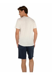 T-shirt di crema chiara a maniche corte con scollo rotondo, abbinata a pantaloni corti blu navy, dotati di due tasche posteriori e una vestibilità comoda.