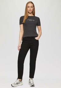 Szara dopasowana koszulka z krótkimi rękawami z haftowanym napisem, w połączeniu z czarnymi dopasowanymi dżinsami i srebrnymi butami sportowymi.