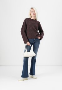 Maglione a maglia bordeaux, jeans blu a campana, borsa bianca e sneakers bianchi. Il maglione ha un colletto rotondo e maniche larghe.