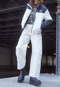 Biała i granatowa kurtka puchowa z wzorzystą górą i spodniami typu cargo w kolorze białym, zestawiona z czarnymi, grubymi butami; gładki materiał, luźny krój.