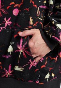 Black sweatshirt featuring a colorful tropical print with pink and white palm trees. Includes a front pocket and ribbed cuffs.