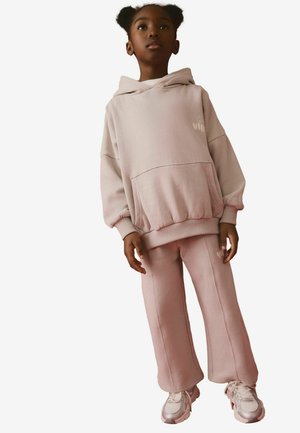 Sweatshirt rose clair avec une poche avant et une capuche, associé à un pantalon de survêtement ample assorti. Les deux sont en tissu doux avec des poignets côtelés.