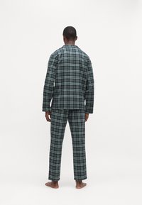 Καρό πιτζάμες φτιαγμένες από μαλακό ύφασμα, με πράσινο, μαύρο και μπλε καρό σχέδιο. Χαλαρή εφαρμογή με μακριά μανίκια και παντελόνια.