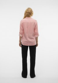 Chemise à rayures rouges et blanches avec des manches retroussées, portée avec un pantalon évasé noir, vue de dos sur fond clair.