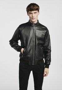 Czarna skórzana kurtka bomberka z zamek błyskawicznym, ściągaczami przy mankietach i dolnej krawędzi. Posiada boczne kieszenie i stojący kołnierz dla dodatkowego ciepła.