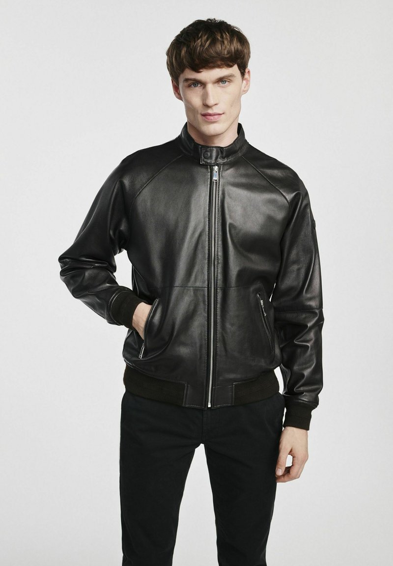 Czarna skórzana kurtka bomberka z zamek błyskawicznym, ściągaczami przy mankietach i dolnej krawędzi. Posiada boczne kieszenie i stojący kołnierz dla dodatkowego ciepła.