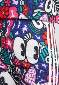 Färggfullt tyg med stora tecknade ögon, röda och rosa blommor, lila och blå abstrakta former samt vita ränder längs sidan.