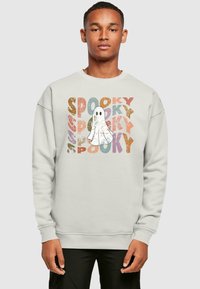 Svetlo sivá mikina so grafikou ducha obklopenou slovom "SPOOKY" v rôznych farbách a s opotrebovanými textúrami. Voľný strih s rebrovanými manžetami.