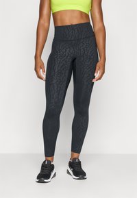 Sorte leggings med et tekstureret leopardprint mønster og en høj talje, parret med en lys grøn crop top og sorte træningssko.
