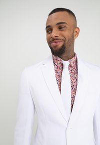 Blazer blanco de corte ajustado, llevado sobre una camisa floral multicolor, complementado con una corbata blanca. Tejido suave con un diseño moderno.