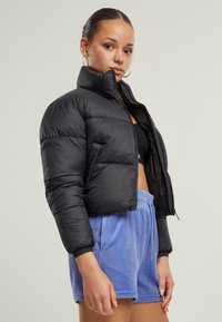 Svart pufferjakke med cropped design, høy krage og glidelås. Kombinert med lyseblå, myke shorts med elastisk midje.