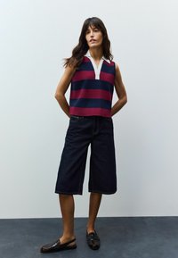 Top sans manches en coloris contrastés avec des rayures bleu marine et bordeaux, doté d'un col blanc. Associé à des culottes en denim foncé à jambes larges et des mocassins noirs.