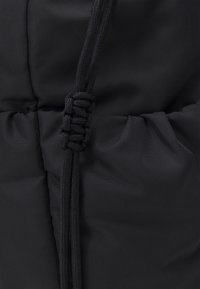 Černá polstrovaná tkanina s texturovaným povrchem, vybavená černým stahovacím šňůrkem a shrnovacím šitím pro úpravu střihu.