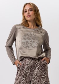 Haut à manches longues en satin taupe avec un motif l�éopard arrondi et clouté, associé à un pantalon brun à motifs présentant un imprimé animal similaire.