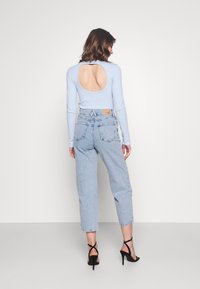 Světle modrá košile s dlouhým rukávem a velkým výřezem na zádech, kombinovaná se světle modrými denimovými džíny s vysokým pasem a černými sandály na vysokém podpatku se pásky.