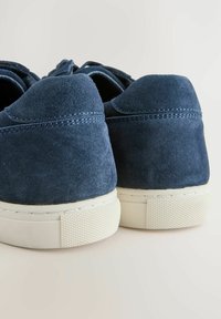 Mørkeblå ruskinds sneakers med en struktureret overflade, hvide gummisåler og kontrasterende syninger, der fremviser et afrundet bagside design.