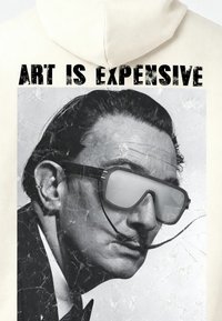 Sweat à capuche crème présentant un portrait en noir et blanc d'un homme moustachu portant des lunettes de soleil surdimensionnées et réfléchissantes, avec le slogan "L'ART EST CHER" au-dessus.