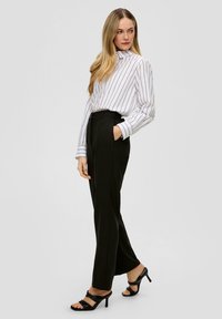 Wit en zwart gestreepte blouse met een hoge hals, gecombineerd met hoge zwarte broeken. Zwarte hak sandalen maken de outfit af.
