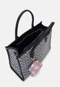 Sac fourre-tout avec un motif zigzag en gris et noir, agrémenté d'une lisière en cuir noir et de deux poignées. Comprend une petite pochette ronde avec un design géométrique rose.