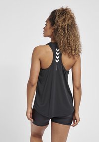 Black sleeveless athletic tank top with a slightly curved hem and a reflective chevron design on the back. Paired with black shorts.