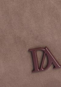 Fondo de material de ante marrón con un destacado logo plástico 'DA' en color burdeos situado en el lado derecho. Textura suave y detalles mínimos.