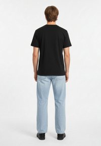 Černé bavlněné tričko s krátkým rukávem, jednoduchý design na zadní straně; doplněno světle modrými džíny a černými botami, minimalistický styl.